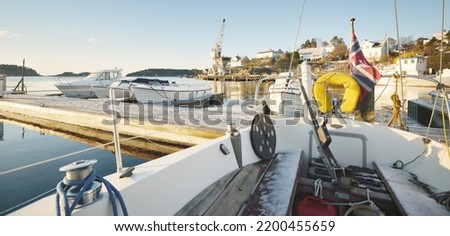 Winterized sloop rigged yachts and cutters moored to a snow-covered pier. Port crane in the background. Norway. Nautical vessel, transportation, sport, recreation, leisure activity, service Royalty-Free Stock Photo #2200455659
