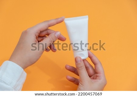 Cosmetic tube in hand in white coat with orange background. Cosmetics, beauty, medicine and spa concept