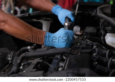 Auto mechanic working and repair on car engine in mechanics garage. Car service. male mechanic repairs car in garage. Car maintenance and auto service garage concept. Royalty-Free Stock Photo #2200457533