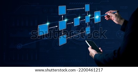 A man's left hand holds a phone, while his right hand holds a pencil, with his power pointing at a 3D monitor where a flowchart is utilized to automate company processes and workflows.