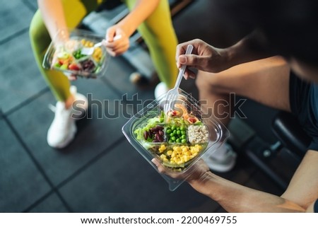 Top view Asian man and woman healthy eating salad after exercise at fitness gym. Two athlete eating salad for health together. Selective focus on salad bowl on hand. Royalty-Free Stock Photo #2200469755