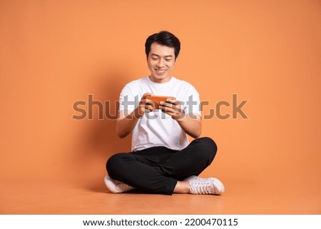 image of asian man sitting using phone and isolated on orange background Royalty-Free Stock Photo #2200470115