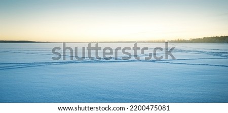 Frozen forest lake at sunrise, trees in a hoarfrost, ski and human tracks in a fresh snow. Idyllic rural scene. Clear blue sky, golden sunlight. Nature, ecology, global warming, Christmas themes