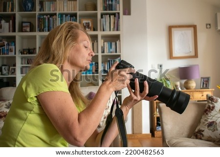 A woman adjusts a long lens DSLR camera. An attractive blonde lady looks at the back screen before she composing a photograph. sharp focus on the lady with soft focus on the colorful room behind