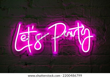 Lets party pink glowing neon sign banner on brick wall