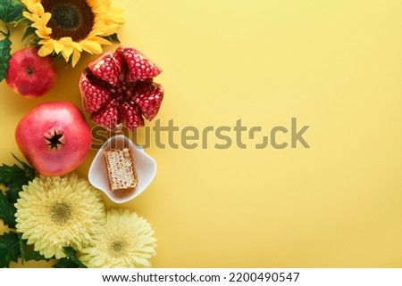 Rosh Hashanah. Ripe pomegranate, apple, honey and sunflower, yellow flowers on yellow background. composition with symbols jewish Rosh Hashanah holiday attributes. Top view with copy space.