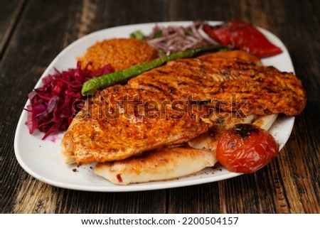 
Grilled chicken breast. Fried chicken fillet with onions, bulgur, roasted green pepper, and roasted tomato on a white plate. Delicious Grilled chicken breast.