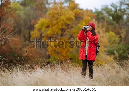 Beautiful woman taking pictures  in the autumn forest. Smiling woman enjoying autumn weather. Rest, relaxation, lifestyle concept.