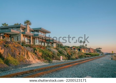 Houses at Del Mar Southern California along railroad on the beach at sunset. Facade of upscale seaside homes overlooking the shore, blue sky, railway, and sea. Royalty-Free Stock Photo #2200523171