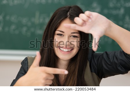 Creative young woman making a frame gesture with her hands as she visualises a project or composes an image looking through her fingers with a beautiful wide smile