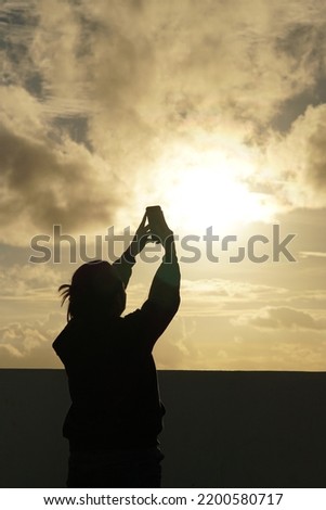 Silhouette of a woman taking selfie photo against the sun 