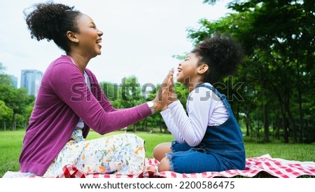 Loving African mom laughing caressing touching hand with cute kid daughter sitting on grass park, happy mother and little child girl hugging having fun playing enjoy funny moments good time together. Royalty-Free Stock Photo #2200586475