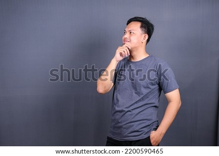 Handsome asian man wearing grey tshirt over grey background looking confident at the camera. Thinking concept