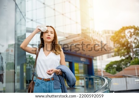 Angry female having sunstroke skin damage from sun UV city air pollution outside on street, Overheating Asian beautiful business woman drying sweat her face with cloth in warm summer day hot weather Royalty-Free Stock Photo #2200592059