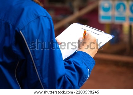 A safety supervisor or manager is writing down on paper for taking note during safety audit at the operation work site. Industrial safety working action scene, close-up and selective focus. Royalty-Free Stock Photo #2200598245