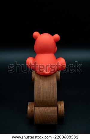 red toy animal riding on top wooden toy car going away, wooden toy car made from cherry wood, isolated on a black background, back view, back of car, concept, driving, parking