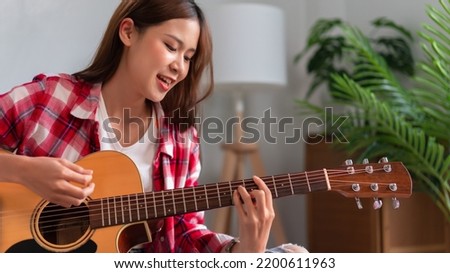Hobby concept, Young asian woman learning and practice playing chords with acoustic guitar on couch. Royalty-Free Stock Photo #2200611963