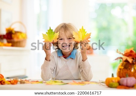 Autumn home decoration. Family decorating house with colorful maple leaves banner. Thanksgiving or Halloween celebration in white living room. Child with fall leaf. Creative crafts ideas with foliage.
