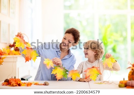 Autumn home decoration. Family decorating house with colorful maple leaves banner. Thanksgiving or Halloween celebration in white living room. Child with fall leaf. Creative crafts ideas with foliage.