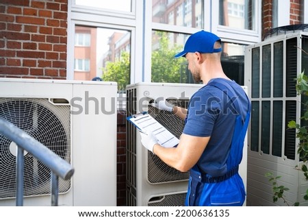 Two Electricians Men Wearing Safety Jackets Checking Air Conditioning Unit On Building Rooftop Royalty-Free Stock Photo #2200636135