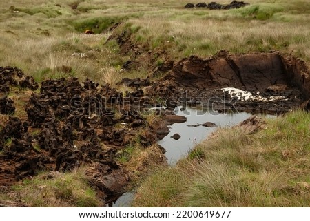 Small piles of Irish peat bog turf in a field air drying for later use in a stove or fireplace as fossil fuel. Use of old not eco friendly heating source during crisis. Retro way to heat home. Royalty-Free Stock Photo #2200649677