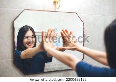 Young adult smile asian woman practice self talk conversation with mirror. Mental health in bathroom at home. Healthy lifestyle after wake up life with satisfaction concept. Royalty-Free Stock Photo #2200658183