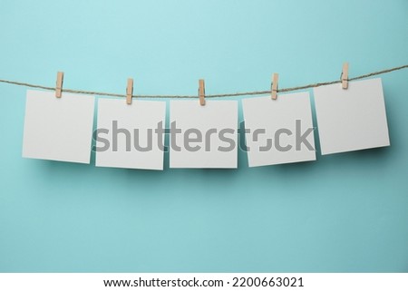 Wooden clothespins with blank notepapers on twine against light blue background. Space for text