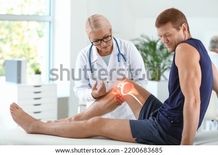 Mature doctor giving sporty man with joint pain injection in clinic Royalty-Free Stock Photo #2200683685