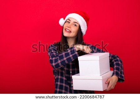 A young cheerful woman in festive pyjamas holds New Year's gifts on a red background in the studio