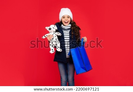 amazed happy kid in puffer jacket and hat. teen girl after shopping on red background.