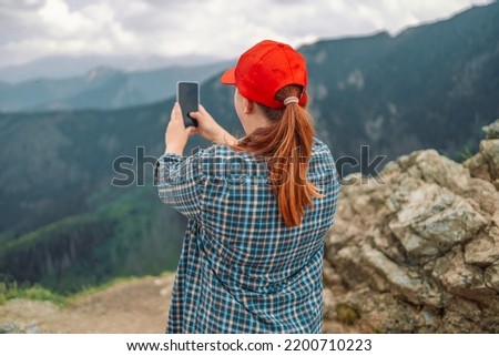 Back view of young beautiful hiker woman taking selfie portrait on the top of mountain, using her smartphone - Hiking and climbing cliff 