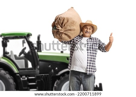 Mature farmer with a sack gesturing thumbs up in front of a tractor isolated on white background
