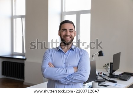 Happy handsome businessman looking at camera, smiling posing with folded hands at office workplace desk. Business startup leader man, CEO, confident professional head shot portrait