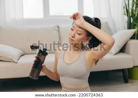 Asian woman at home doing stretching and yoga online and drinking water while resting, wiping sweat from her forehead