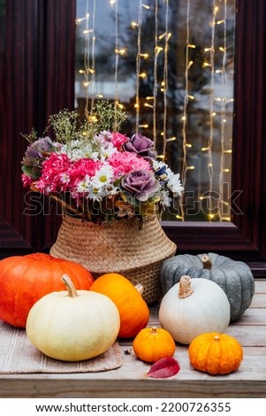 House decorated for autumn holidays. Door illuminated with garland and porch with various pumpkins and flowers in the wicker basket for Thanksgiving or Halloween. Fall Harvesting. Selective focus