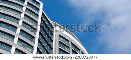 Office skyscraper high business building on blue sky background, looking up tall glass windows and steel high rise modern building. Multistory glass building with cloudy blue sky background