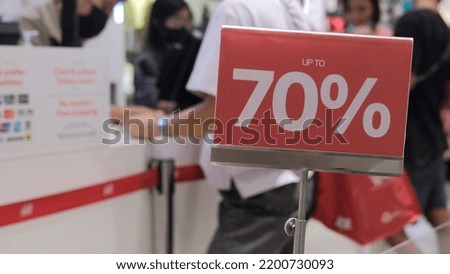 Red sign with a 70 percent discount to attract customers. In the background in blur, unrecognizable customers at the checkout are eager to buy at a bargain price in the store. Discount concept.