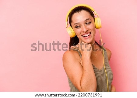Young caucasian woman listening to music isolated on pink background points with thumb finger away, laughing and carefree.