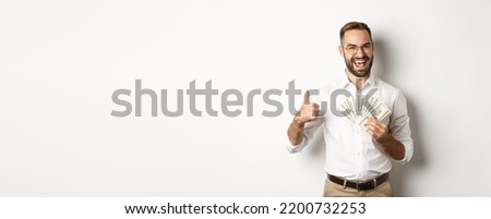 Excited rich man holding money, showing thumb up in approval, standing over white background Royalty-Free Stock Photo #2200732253