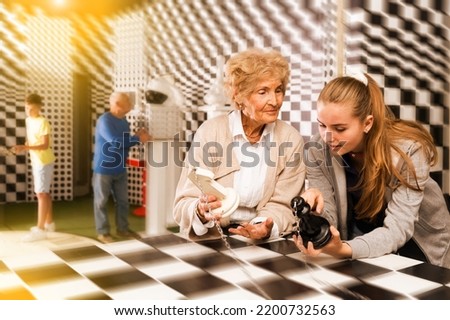 Young girl and her granddaughter solving chess conondrum in escape room. Grandson and grandfather working on another conondrums in background.