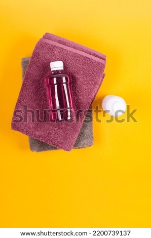 A folded grey and purple towels, a bottle of shampoo and purple shower gel on yellow background.  Bath mockup with copy space.
