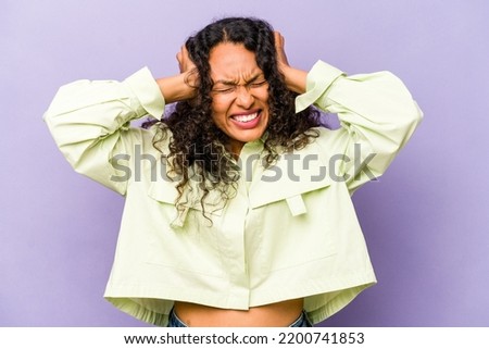 Young hispanic woman isolated on purple background covering ears with hands.