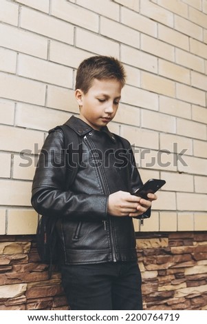Schoolboy with backpack using smartphone, texting outdoors standing on brick wall urban background. Teenager boy playing video game in internet. Social media