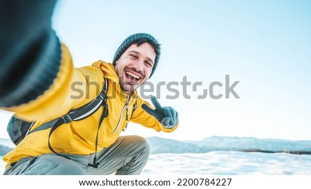 Young man wearing winter clothes taking selfie picture in winter snow mountain - Happy guy with backpack hiking outside - Recreation, sport and people concept Royalty-Free Stock Photo #2200784227