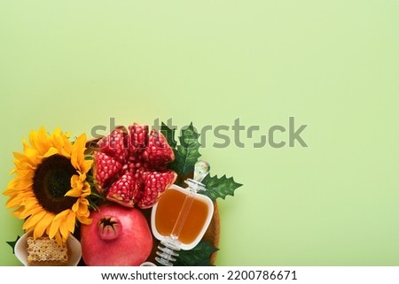Rosh Hashanah. Ripe pomegranate, apple, honey and sunflower, yellow flowers on green background. composition with symbols jewish Rosh Hashanah holiday attributes. Top view with copy space.