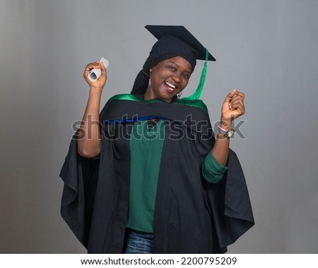 Celebration picture of an African female student or graduand from Nigeria, wearing graduation gown and cap while posing for the camera and celebrating success in education