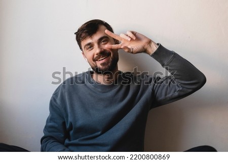 Young guy listening to music using  wireless headphones doing peace symbol with fingers over face, smiling cheerful showing victory, have fun, dancing.
