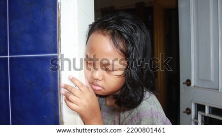 little girl who is tired and sleepy leaning against the wall