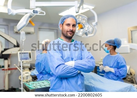 Portrait of male surgeon standing with arms crossed in operation theater at hospital. Team surgeons are performing an operation, middle aged doctor is looking at camera, in a modern operating room