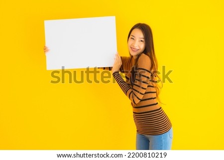 Portrait beautiful young asian woman with empty blank white card board for text on yellow isolated background